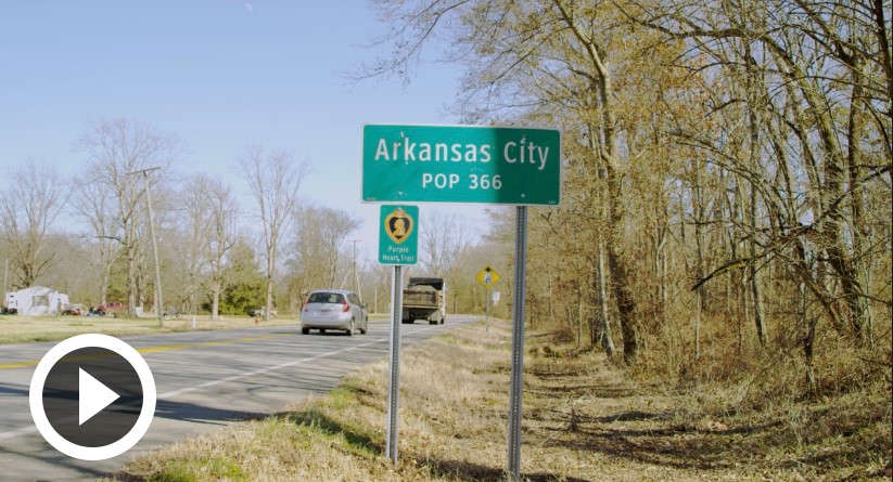 image of road with cars, with green sign on side saying " Arkansas City Pop 366"